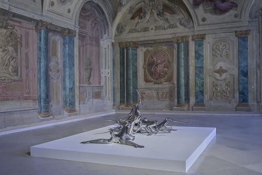 Ausstellungsansicht: Skulptur aus silberfarbenen metallenen Affen auf einem weißen Podest im Carlone Saal des Oberen Belvedere
