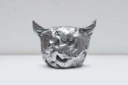 The photo shows a metal sculpture in silver. The shape is reminiscent of a cat's head or devil's head