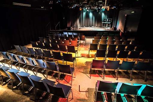 Foto eines Veranstaltungssaals mit Sesselreihen im Vordergrund, einer Bühne im Hintergrund