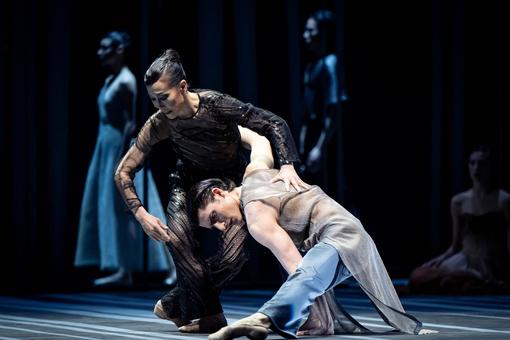Szenefoto aus dem Ballett "Pathétique" der Wiener Staatsoper. Tanzszene mit zwei Solotänzer:innen, die Frau in einem schwarzen Kostüm, der Mann in einem hellen Outfit