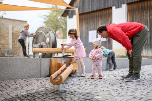 Das Foto zeigt einige Kinder, die am Wasserlehrpfad von Schloss Hof spielen und Wasser in hölzenen Rinnen umleiten
