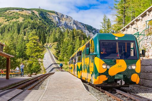 Photo of the green-orange Salamander train standing in the mountain station on the Schneeberg, in the background the mountain landscape