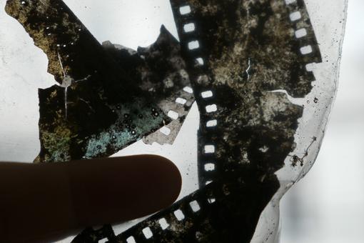 The photo shows crumpled and partially broken photo negatives and the black shadow of a finger pointing at them.