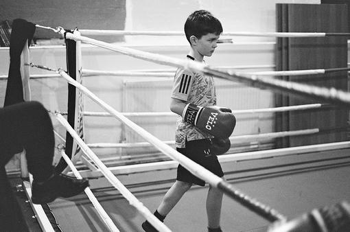 Black and white photo of small boy with big boxing gloves in boxing ring