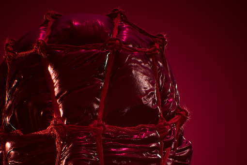 The photo, completely bathed in Bordeux red, shows the upper section of a sculpture of a large head wrapped and tied up in plastic