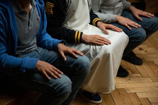 The photo shows the hands of three young men placed palm down on their knees.