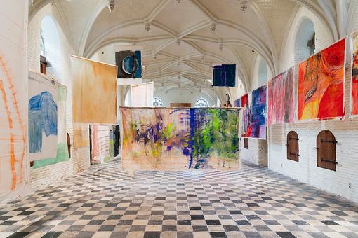 Exhibition view: colorful abstract canvases hanging freely on poles in a high room with vaulted ceiling