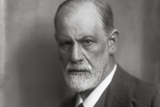 A portrait photo in black and white of Sigmund Freud looking into the camera, the left side of his face is more strongly illuminated
