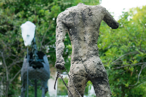 Sculpture of a male torso, view from behind, pulling something behind him on a rope