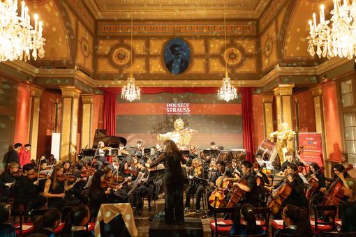 The photo shows a youth orchestra with conductor playing a concert in the ballroom of the House of Strauss in Vienna