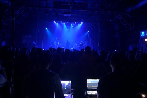 Foto während eines Konzertes einer Band, Blick vom Mischpult aus auf die in blaues Licht getauchte Bühne