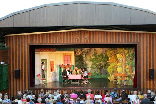 Bühnenansicht der Freiluftbühne, 4 Schauspieler in einer Szene in einem typischen österreichischen Gastgarten, vor der Bühne das Publikum