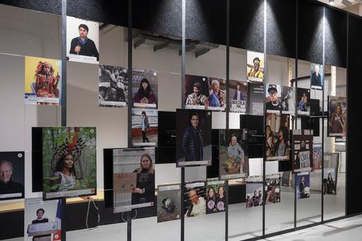 Das Foto zeigt eine Wand der Ausstellung, auf der Fotos unterschiedlicher Größe von Umweltaktivist:innen weltweit gezeigt werden.