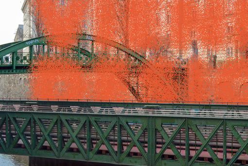 Foto einer historischen Brücke, eine grüne Stahlkonstruktion mit Bogen, darüber in orangeroter Farbe wirkt der Schriftzug Vienna Design nur angedeutet und wie aufgesprüht