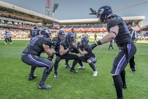 Photo of the Vienna Vikings football players at the start of a game, in the background the stands of a stadium