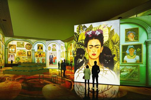 Ausstellungsansicht mit unzähligen immersiven Gemälden von Frida Kahlo, im Vordergrund ein Selbstporträt der Malerin