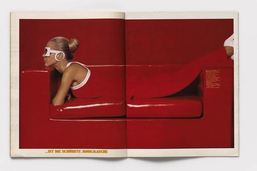 The photo shows a red leather couch on which a woman is lying on her stomach. She is wearing an outfit in the same red color as the couch, with white sunglasses and white shoes. Her blonde hair is pinned up in a bun