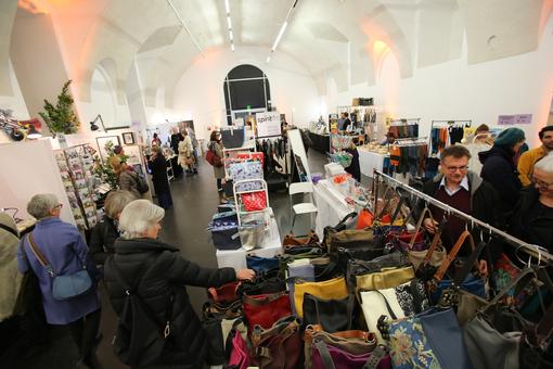 Ausstellungsraum des WeihnachtsQuartier im MQ mit Verkaufsständen und Besucher:innen, im Vordergrund ein Stand mit verschiedenen Designer-Taschen