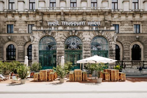 Photo of the main entrance of the Weltmuseum with a guest garden and a large white parasol in front of it