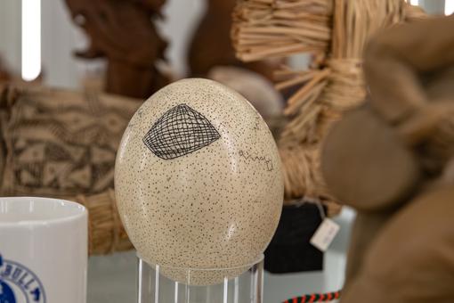 Ausstellungsansicht: Ein auf einem Plastikzylinder stehendes Straußen-Ei, auf dem sich eine gitterartige Zeichnung befindet