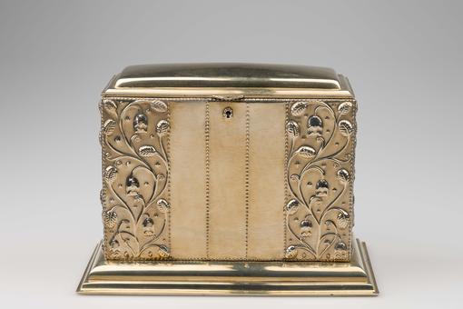 Photo of a silver-plated metal box finely worked and chased, floral tendrils on the side 
