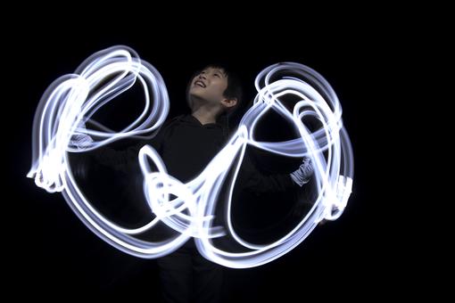 Das Foto zeigt die Bewegung der Arme einer jungen Japanerin wie weiße Lichtschlangen vor schwarzem Hintergrund