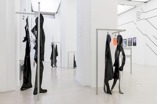 Exhibition view with black silhouettes made of plastic foil hanging on metal bars
