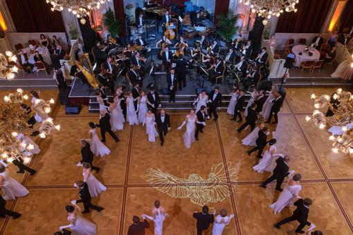 The photo shows a bird's eye view of a scene from the ball opening: dancing couples in white, floor-length evening gowns and black suits and the ball orchestra