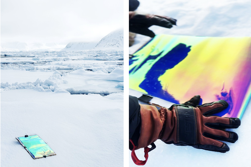 Das Foto zeigt die Arbeit von Laure Winants mit Licht und Farbe in der Arktis. Zu sehen ist ein färbiger Print der von dicken rotschwarzen Handschuhen gegen das Eis gehalten wird. 