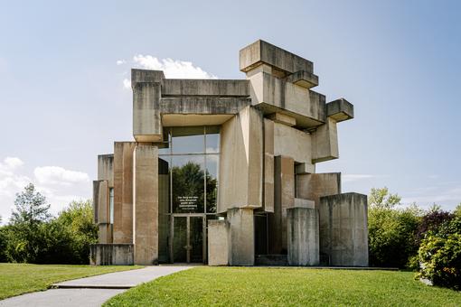 Photo of a modern church, built as if from individual concrete blocks, entrance portal is a high glass front with beam struts