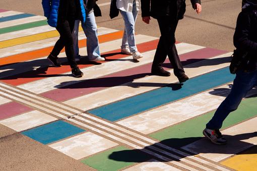 The photo shows a crosswalk in the colors of the rainbow and the feet and legs of some passers-by