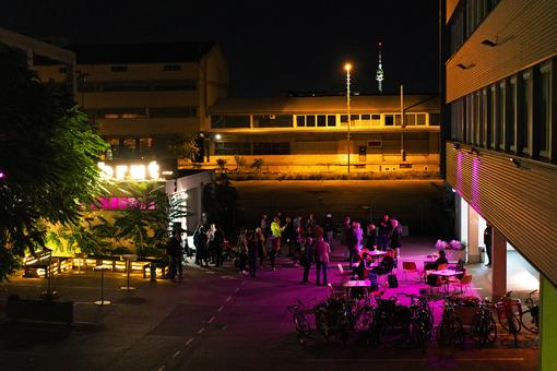Photo at night, season opening of brut nordwest, a crowd is standing in front of the building, a pub garden is bathed in pink light