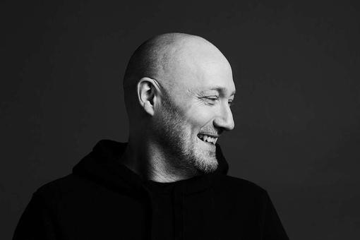 Portrait photo of Paul Kalkbrenner in black and white, looking down to the left and smiling.