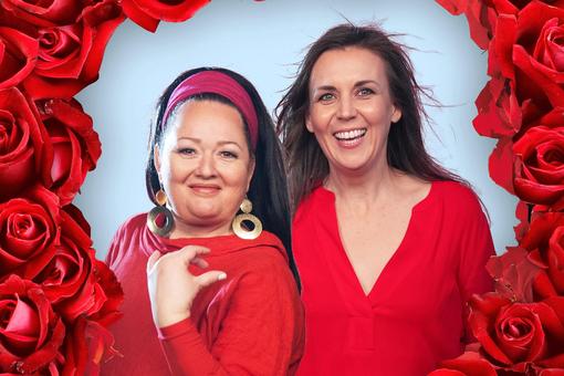 Das Foto zeigt die Musiker:innen und Sänger:innen Tini Kainrath und Maria Stippich in roten Kleidern, umrahmt von roten Rosen