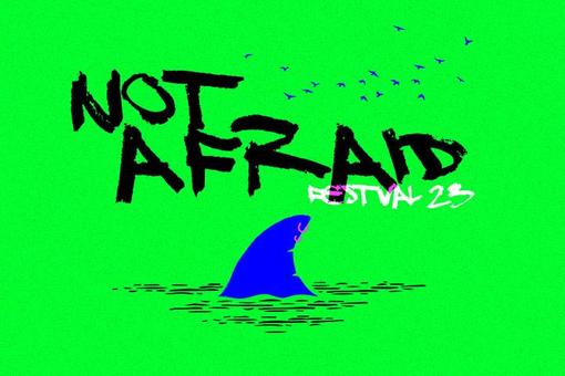 The lettering "Not Afraid Festival 2023" in black and white color, below a blue shark fin sticking out of the water, rich green as background