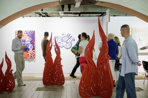 Ausstellungsansicht aus der Kunstmesse im Jahr 2022: flammenähnliche rote Skulpturen, dazwischen Besucher:innen