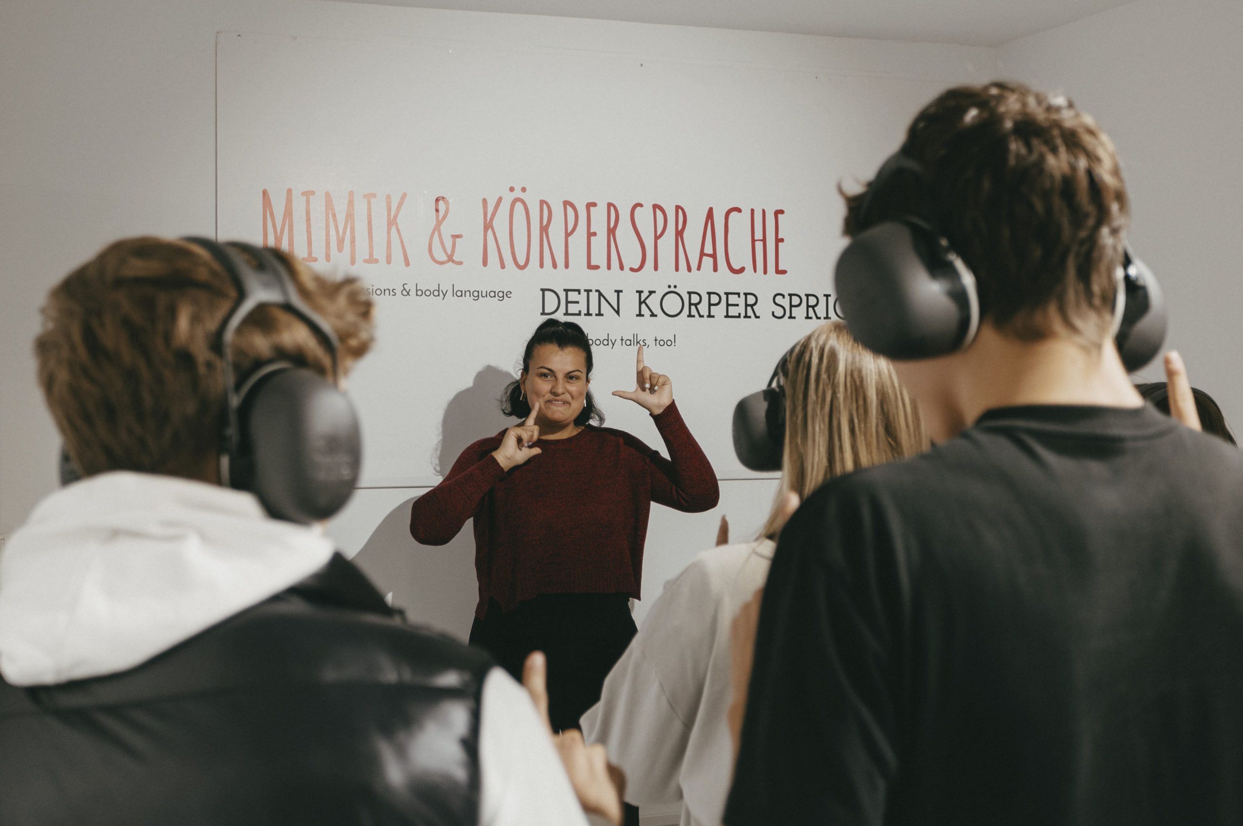 © HandsUp / Foto: Gerd Schneider Photo of young people with headphones taken from behind. In front of the group is a young woman speaking in sign language