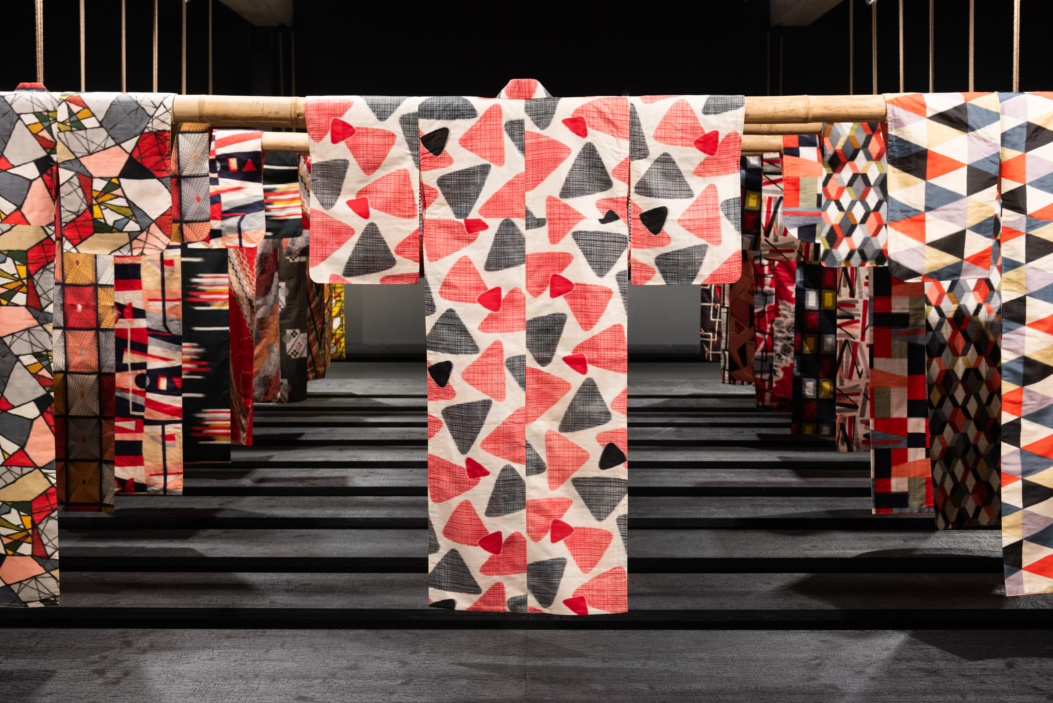 Ausstellungsansicht MAK 2025: MUSTER DER MODERNE. Meisen-Kimonos aus der MAK Sammlung – Schenkung Friis © MAK / Stella Riessland Die Ausstellungsansicht zeigt zahlreiche auf Bambusstangen hängende Meisen-Kimonos mit unterschiedlichen Mustern und Farbkombinationen