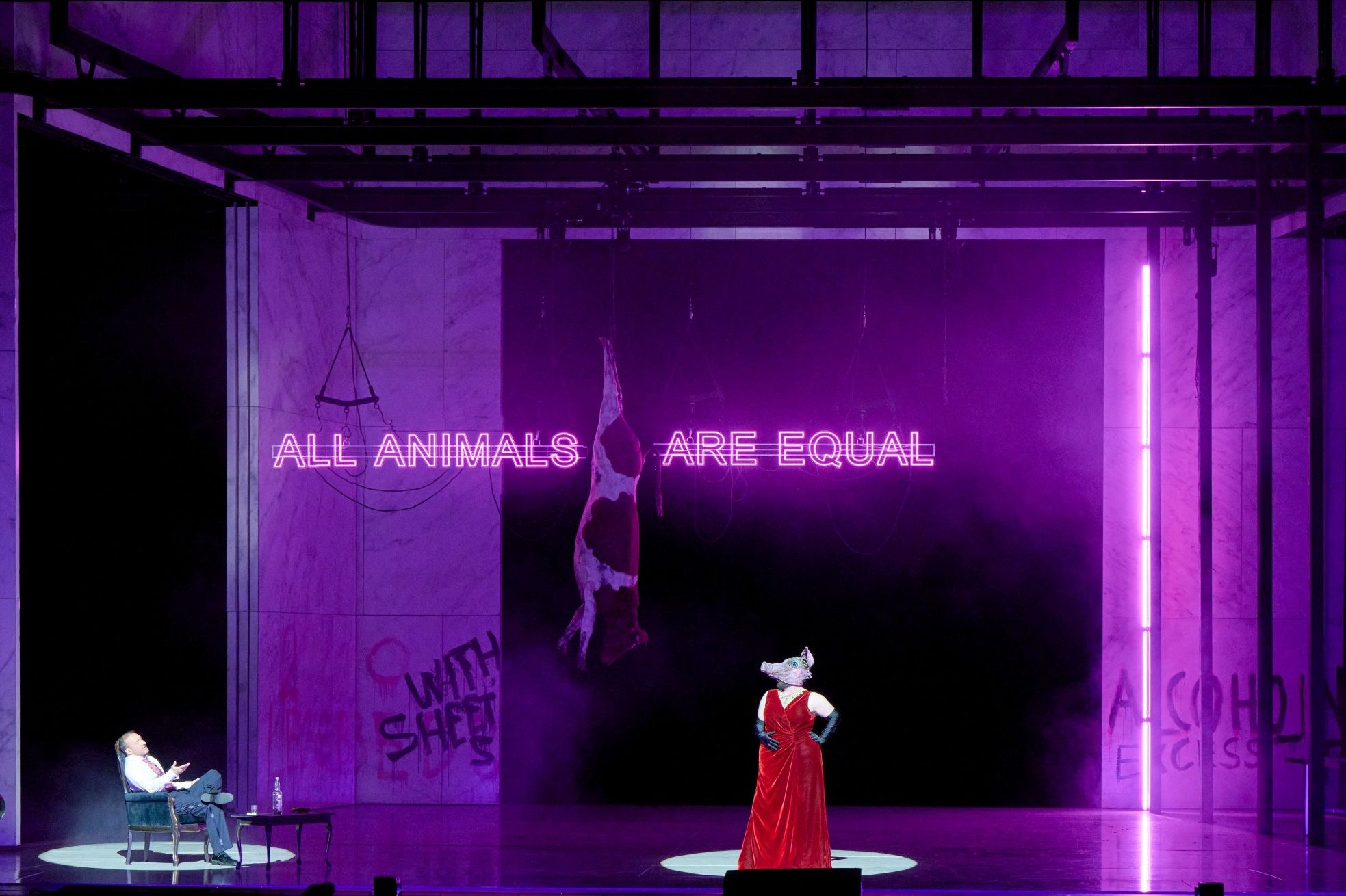 Wiener Staatsoper / Animal Farm © Foto: Michael Pöhn Eine Figur mit Schweinemaske steht in rotem Gewand im Zentrum einer lila beleuchteten Bühne, hinter ihr leuchtet der Satz „ALL ANIMALS ARE EQUAL“.