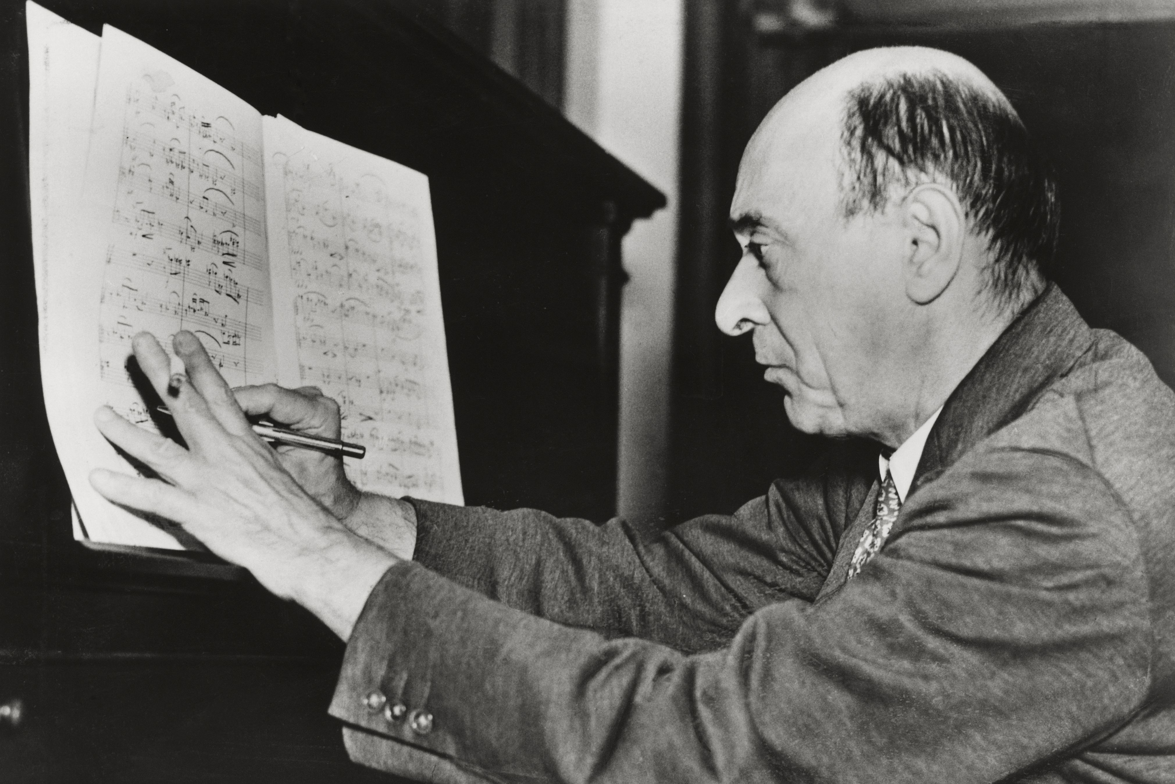 Arnold Schönberg, Los Angeles, ca. 1935 © A Arnold Schönberg Center Black and white photo of Arnold Schoenberg sitting at a piano and writing notes in a patitur