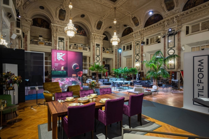 Foto: © Design District AD Werbe Design Atelier GmbH Exhibition view with various design furniture, in the foreground a brown wooden dining table with four blackberry upholstered chairs