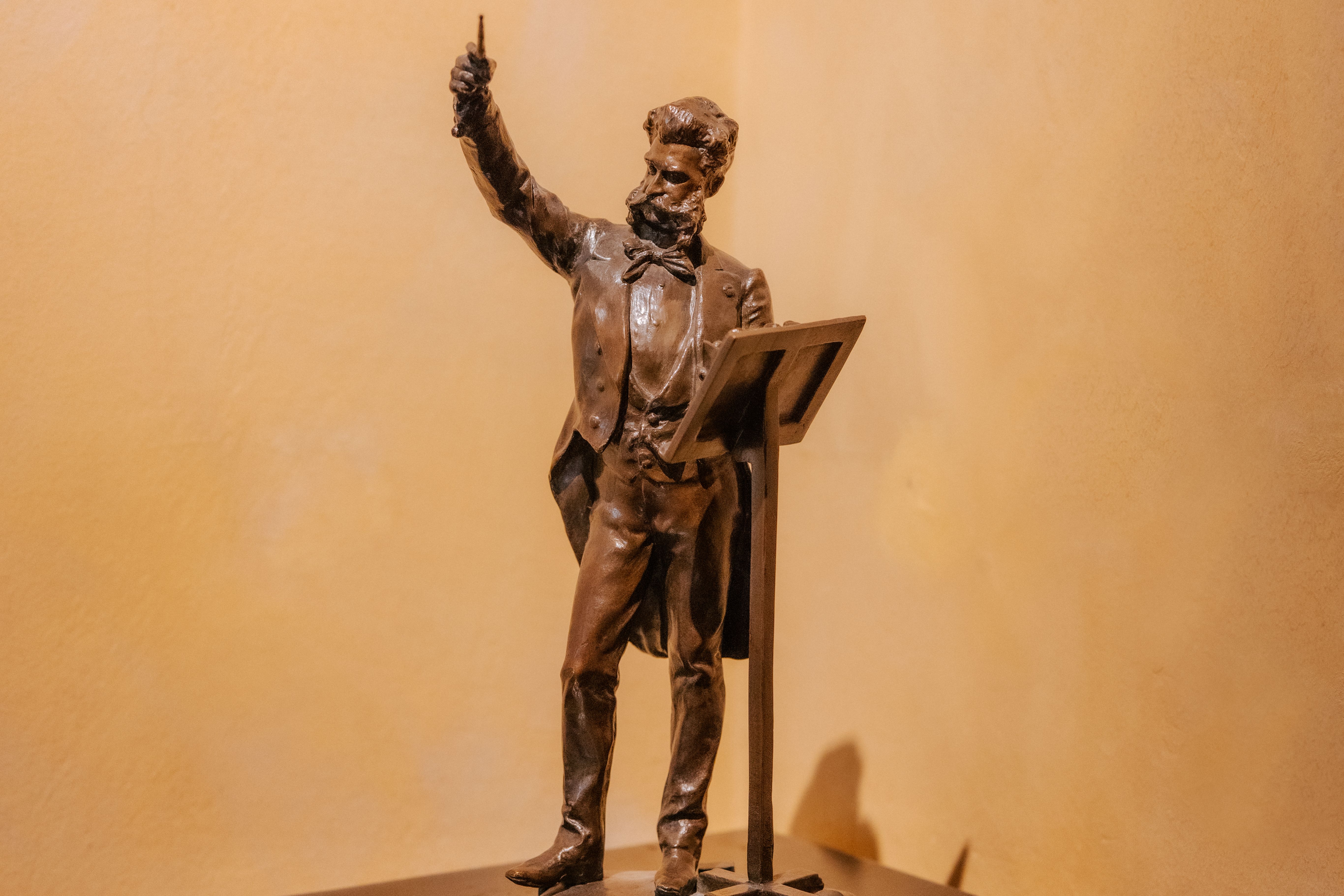 @ WienTourismus / Paul Bauer Das Foto zeigt eine braune Statuette es Komponisten Johann Strauss. Johann Strauss steht in einem Frank an einem Pult und dirigiert