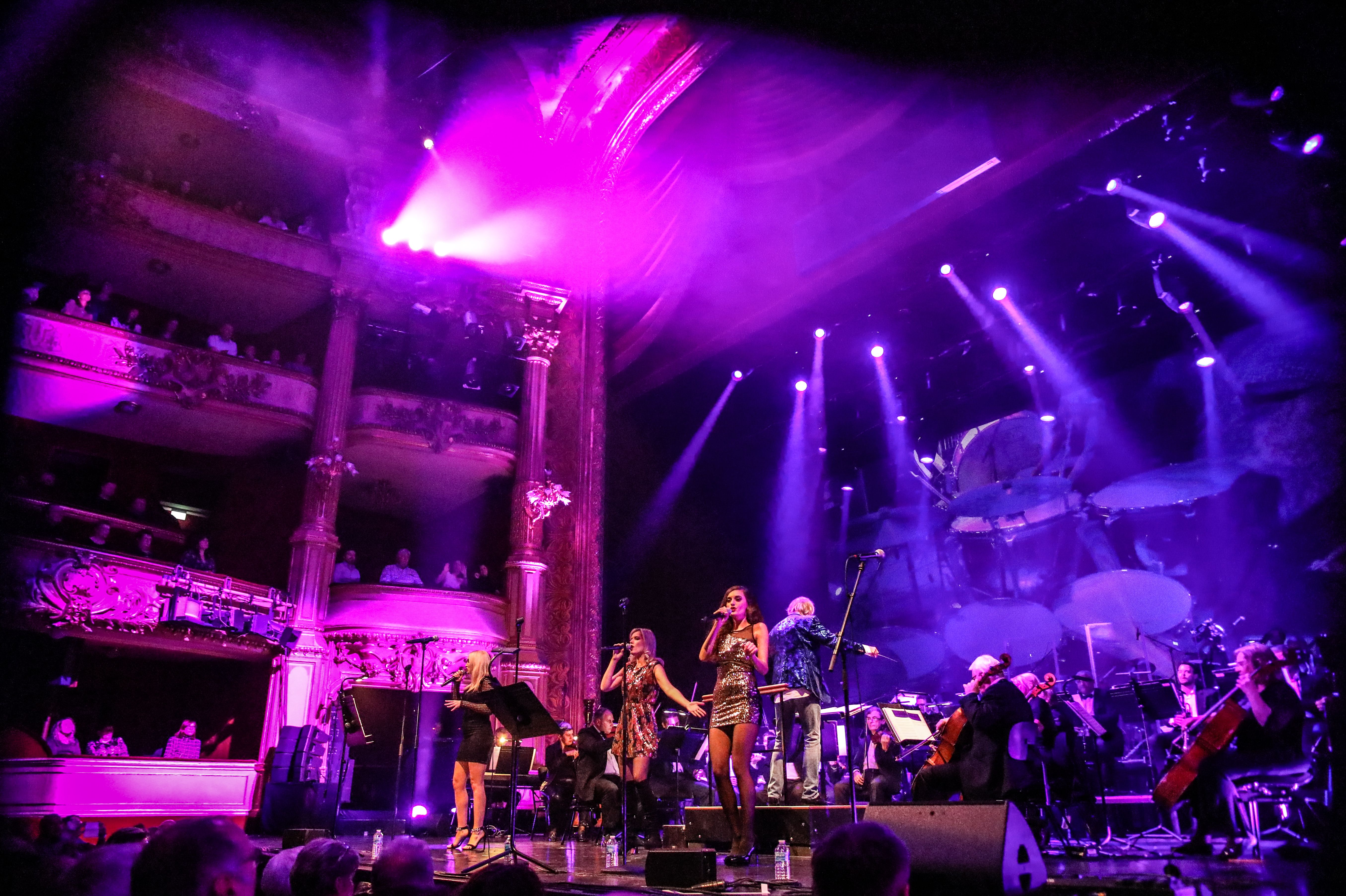 Foto: © Prague Classics s.r.o. Photo with scene of the show on the stage of the Vienna State Opera, the orchestra in the background, three singers in the foreground, the scene bathed in magenta light