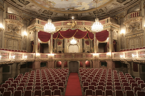 Foto: © mdw © 2023 Institut für Gesang und Musiktheater / Verena Soltiz Foto des barocken Innenraums des Schlosstheaters mit erleuchteten Kristall-Lustern, Balkonen und der Bestuhlung im Parterre