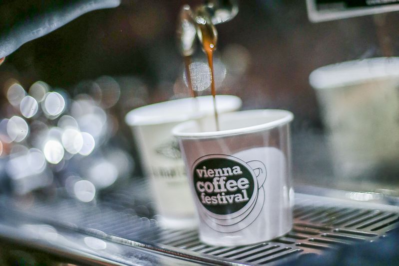 Photo of a coffee mug with the logo of the Vienna Coffee Festival into which freshly brewed coffee runs