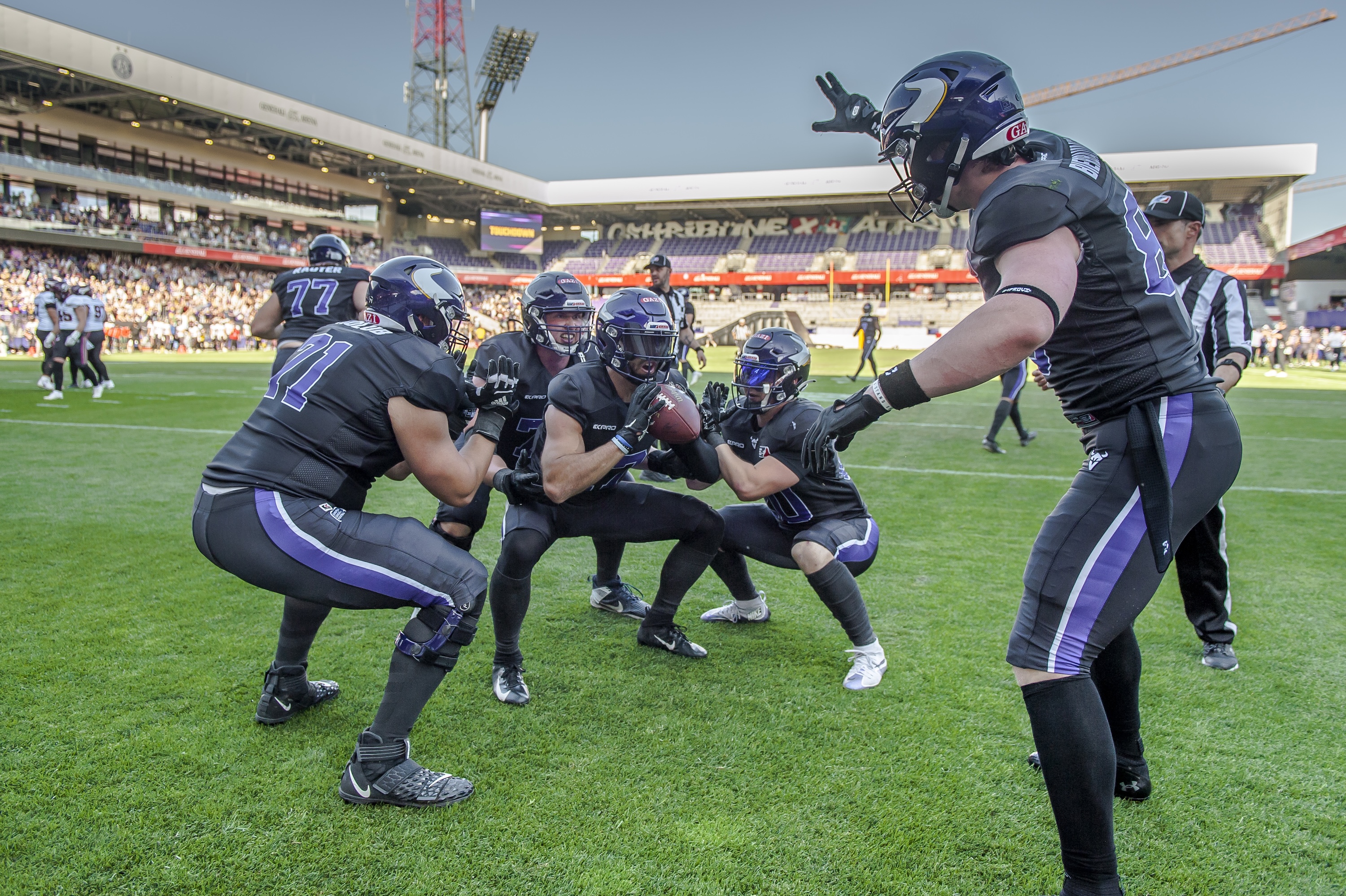 Foto: © Vienna Vikings Foto der Vienna Vikings Football Spieler beim Start zu einem Spielzug, im Hintergrund die Tribünen eines Stadions