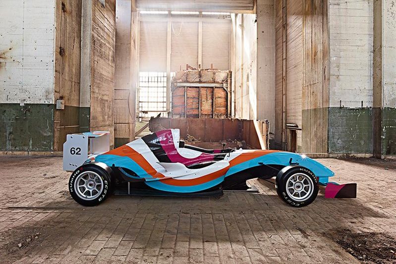 Art Car Sabine Lang, Daniel Baumann / Ferdinand Habsburg @ Kaiserliche Wagenburg, Kunsthistorisches Museum Wien Das Foto zeigt ein künstlerisch gestaltetes Rennauto (Formula Renault 1.6) in den Farben Hellblau, Orange, Weiß, Pink und Schwarz. Das Auto befindet sich in einer Fabrikshalle.