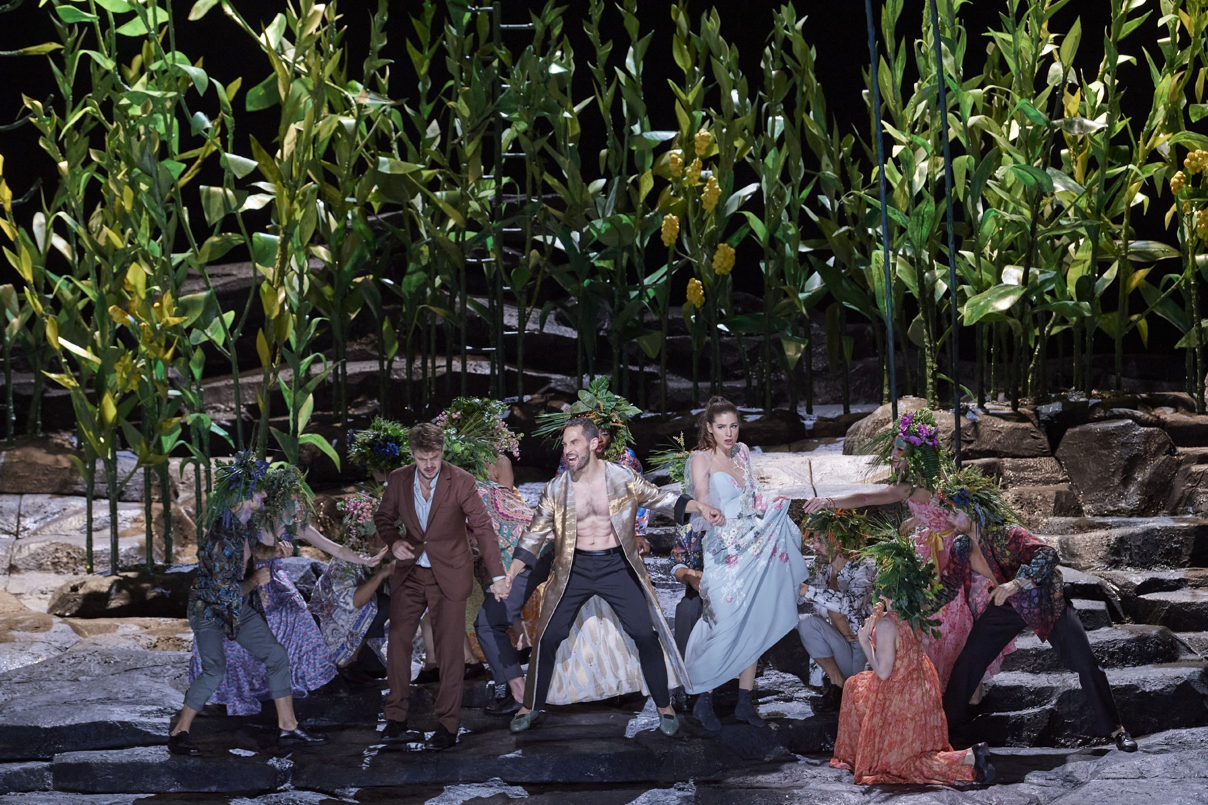 Wiener Staatsoper / Don Giovanni © Foto: Michael Poehn Das Szenefoto aus der Oper "Don Giovanni" zeigt den Hauptdarsteller, der eine Frau und einen Mann an der Hand hält, umgeben von 6-8 Personen mit Pflanzenschmuck auf dem Kopf, im Hintergrund ein Wäldchen aus Pflanzen