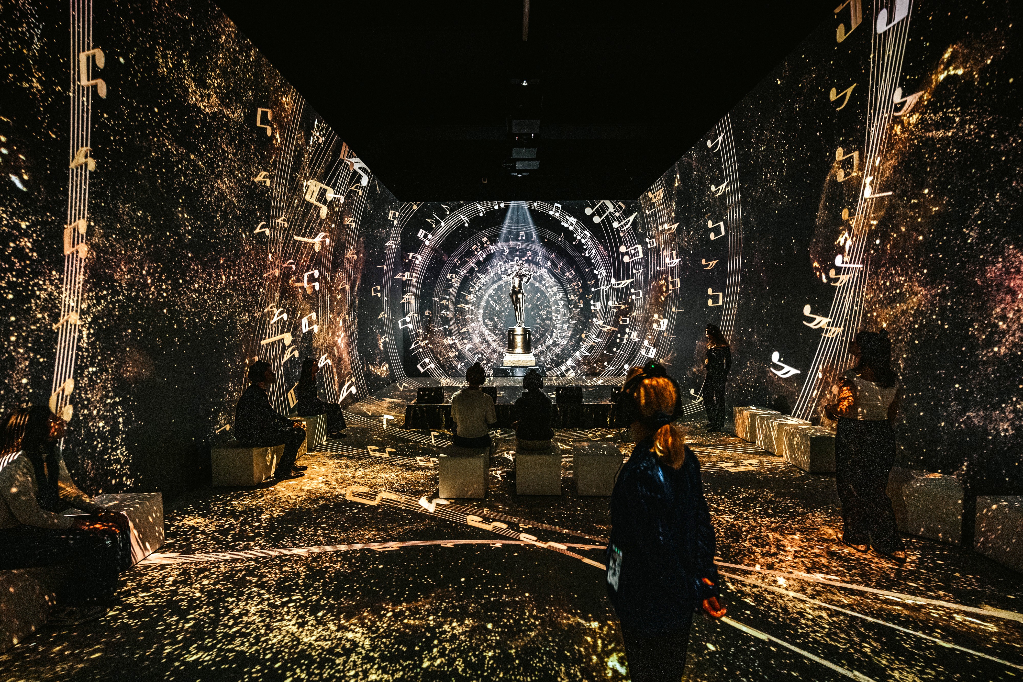 Philipp Lipiarski Ausstellungsraum im Johann Strauss Museum - New Dimensions mit Strauss-Statue und abstrakten Musik-Visuals, darunter auch Notenzeilen sowie Besucher:innen.