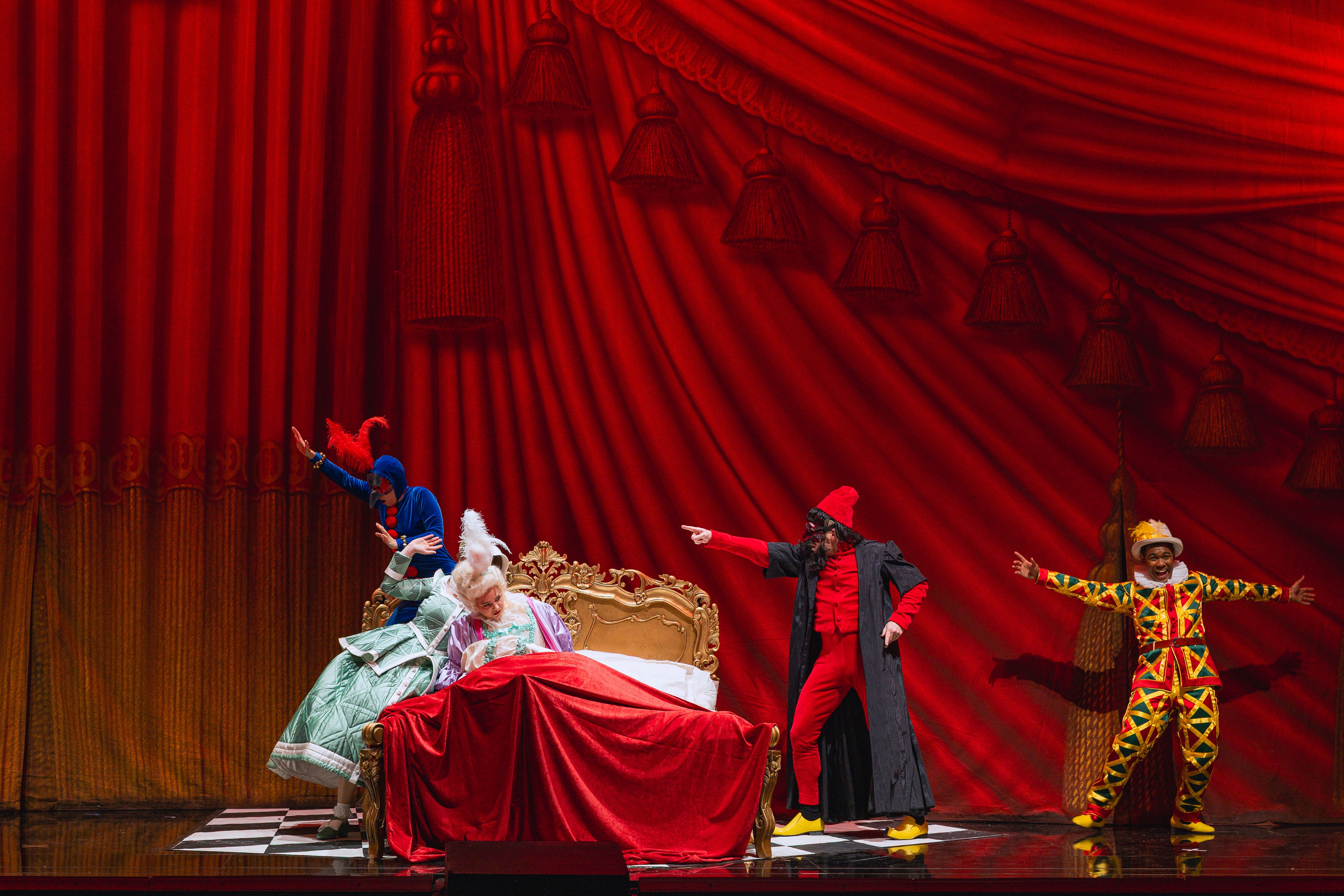 Annelie Sophie Müller (Cherubino), Lauren Urquhart (Susanna), Matilda Sterby (La contessa d´Almaviva), Daniel Schmutzhard (Il conte d´Almaviva), Michael Arivony (Figaro) - © Marco Sommer / Volksoper Wien The scene photo from the opera “Le nozze di Figaro” shows four leading actors in colorful costumes cavorting around a baroque bed with a red bedspread in front of a deep red background that looks like a curtain with folds and tassels